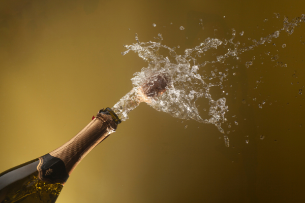 a cork exploding from a champagne bottle with a wave of sparkling wine gushing out