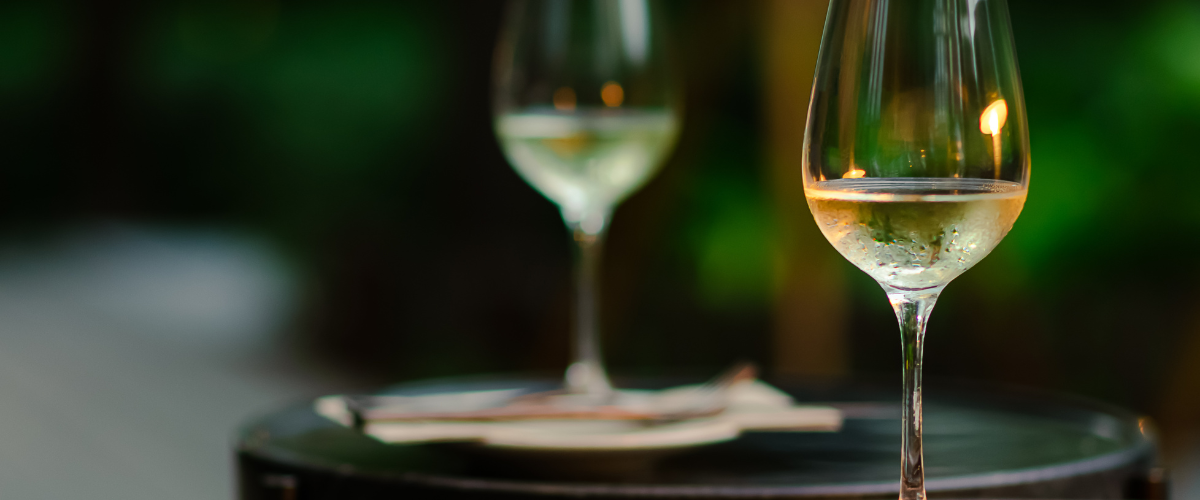 Foreground white wine being poured into a glass; background blurry white wine glass