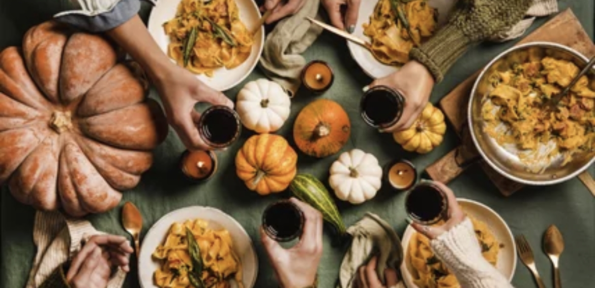 Overhead image of a fall table filled with gourds and 4 red wine glasses coming together to cheers
