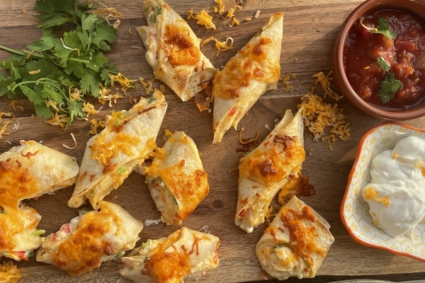 overhead view of a wood board piled with cheesy antojitos, salsa, and cilantro