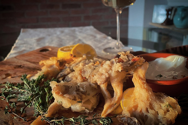 A pile of fried mushrooms on a wood board, a blurry glass of white wine in the back ground