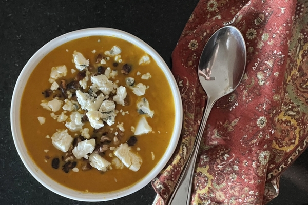 overhead view of a bowl of butternut squash soup on a black background with a fall napkin on the side