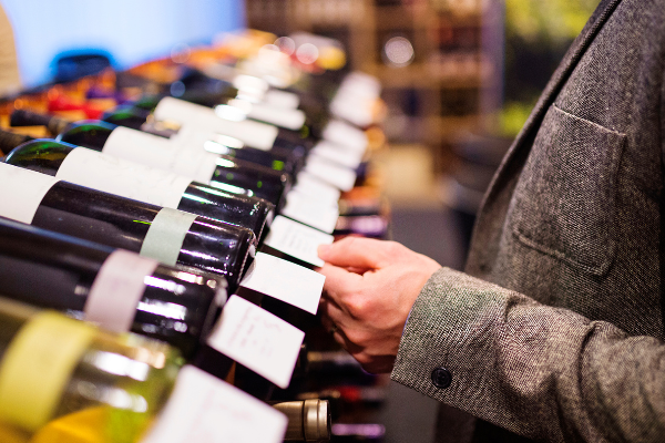 A close up of a wine shelf; a man's hands holding a bottle