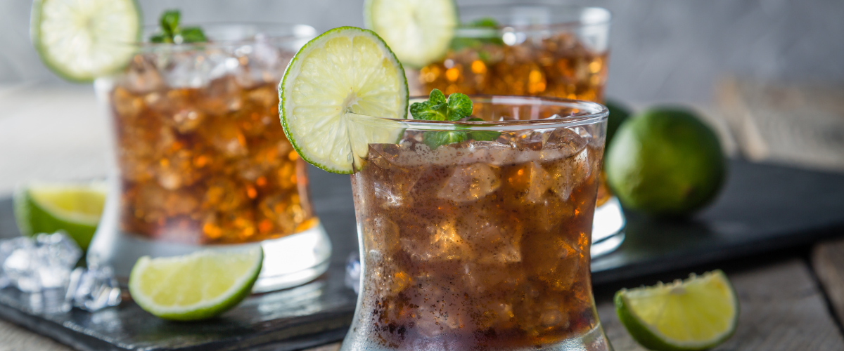 side view of 3 dark n' stormy cocktails, filled with ice, piles of limes around them.