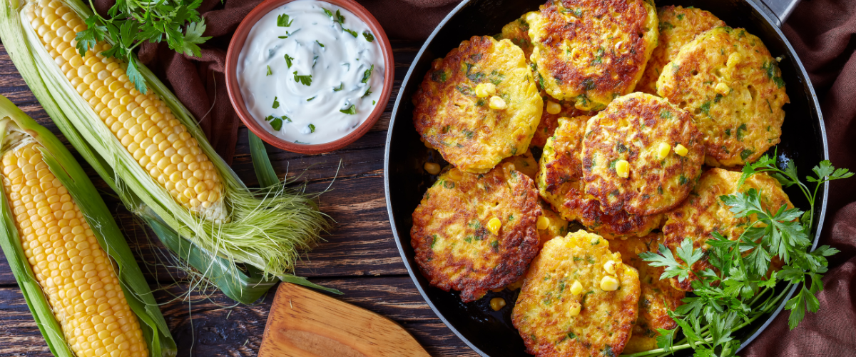 A bowl of corn fritters with a wooden spoon and bowl of ranch on the side