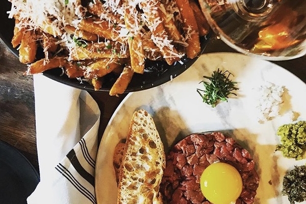 image of steak tartare with egg yolk on top and crostini on the side with french fries and wine beside it