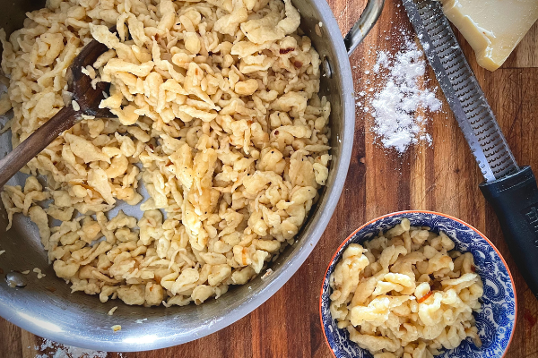 over head view of spätzle in a pan on a wood board. A small bowl of spätzle is beside it.
