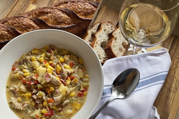 overhead view of a bowl of turkey corn chowder on a wood board with a baguette and glass of white wine
