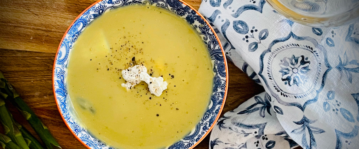 overhead view of asparagus soup in a blue and white bowl on a wood board