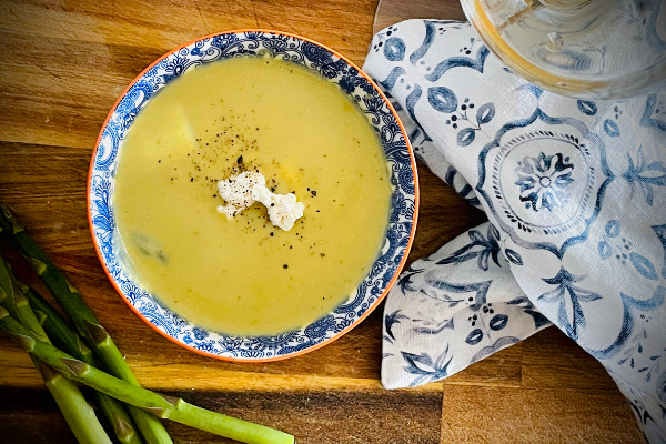 overhead view of asparagus soup in a blue and white bowl on a wood board