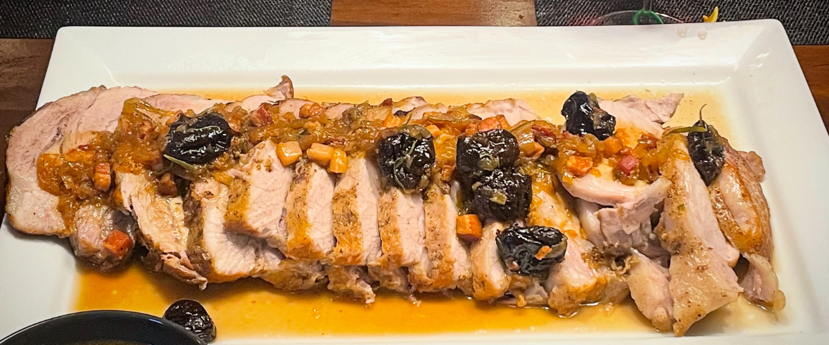 side view of sliced pork on a white plate with prunes and sauce