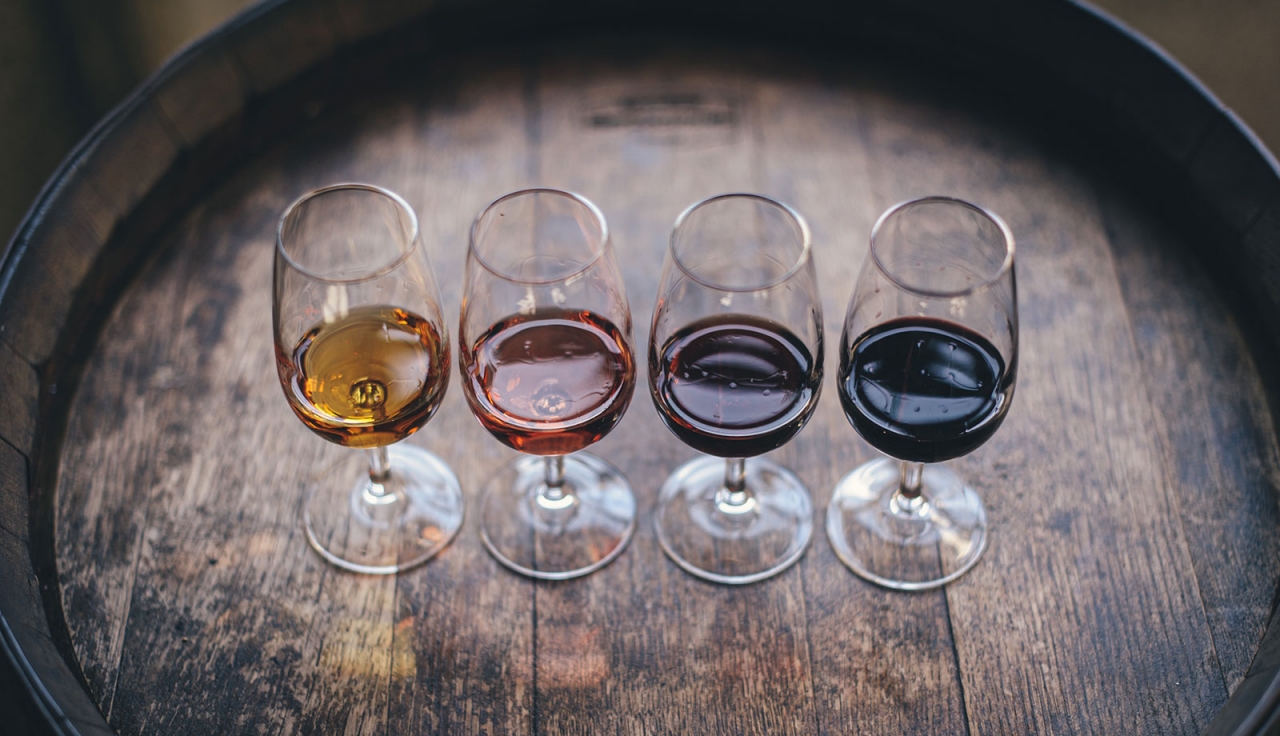 A line up of 4 wine glasses containing white, rosé, and red wine on a wooden wine barrel