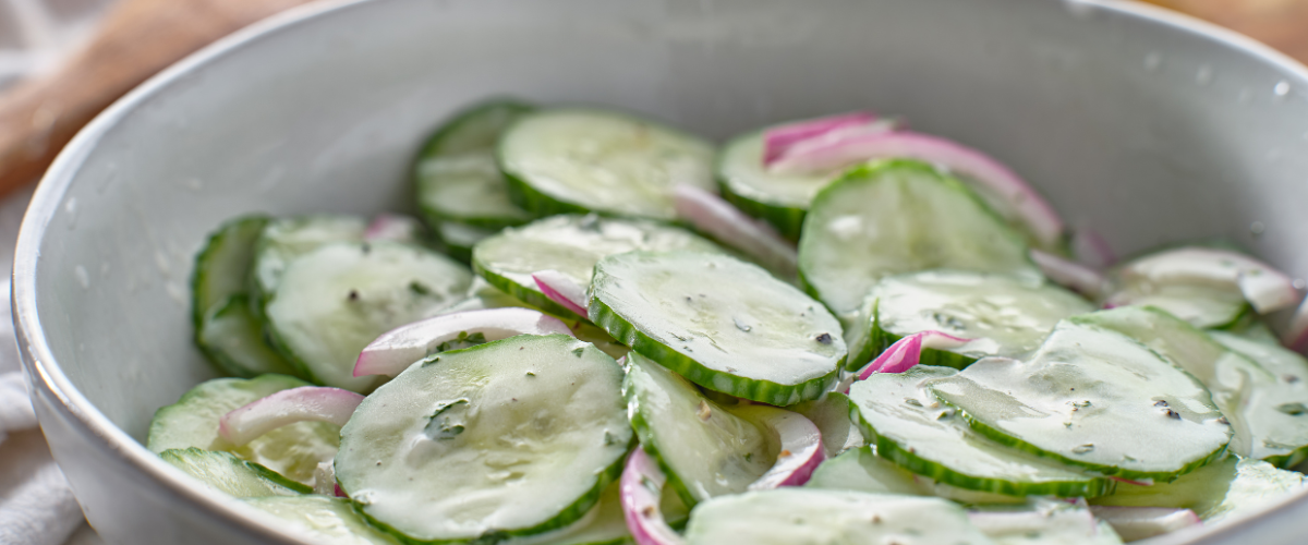 close up side view of creamy cucumber salad in a white bowl
