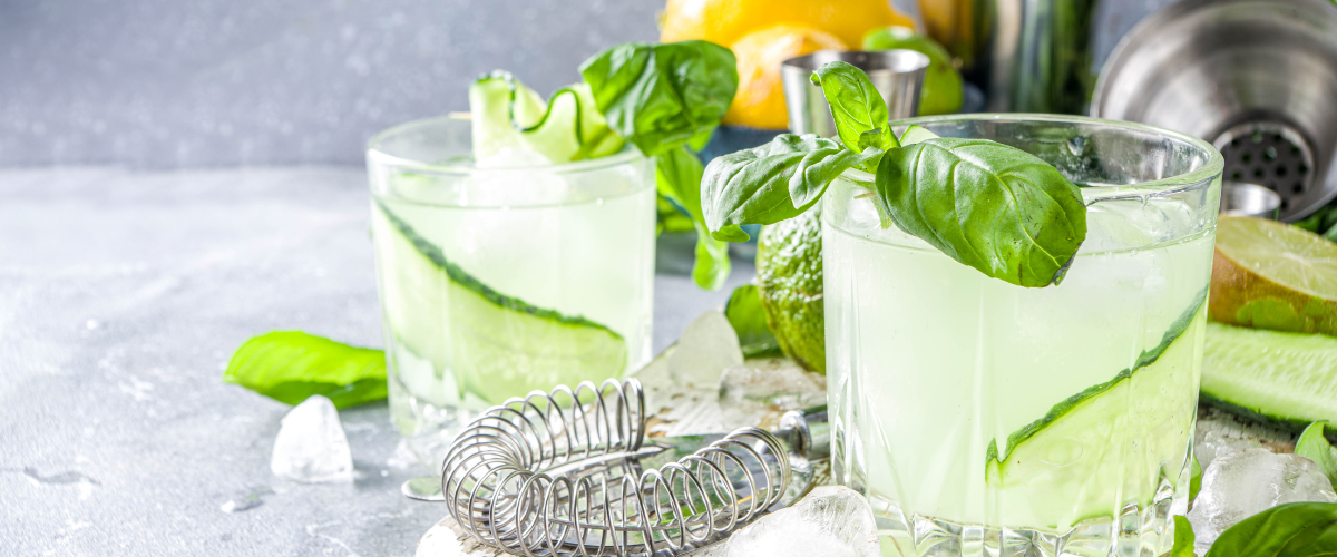 side view of two rocks glasses on a tray filled with cocktail and cucumber garnish