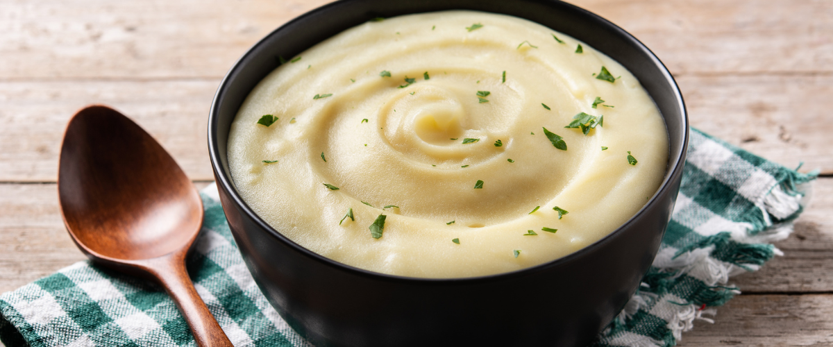 a side view, close up of creamy mashed potatoes in a swirl in a black bowl