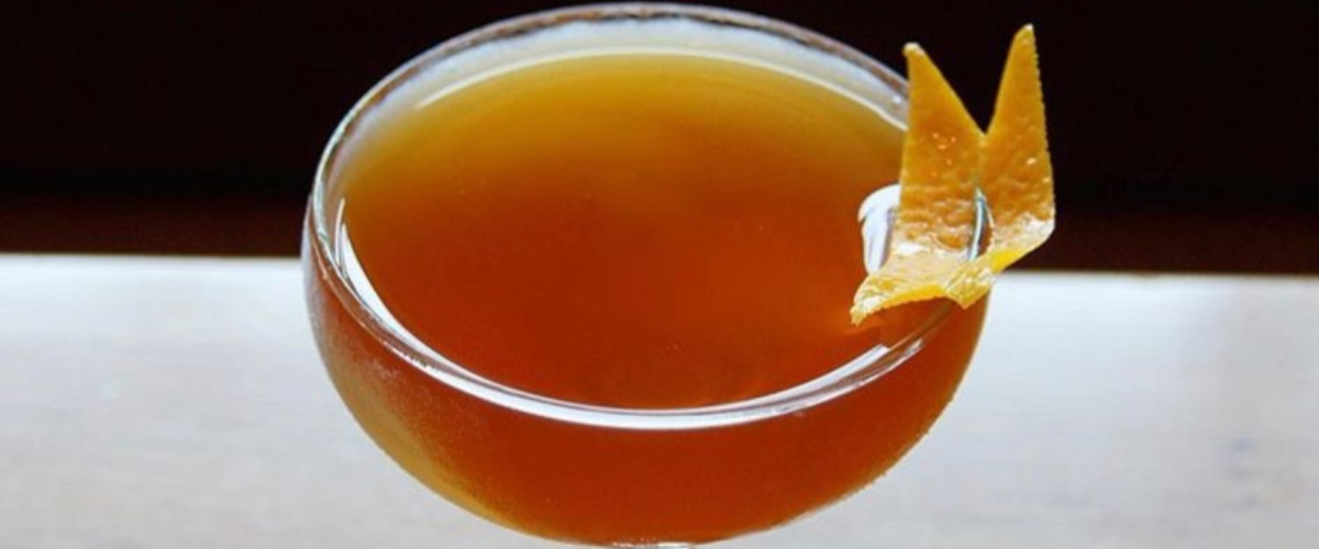 close up of a brown/red cocktail in a coup with an orange twist