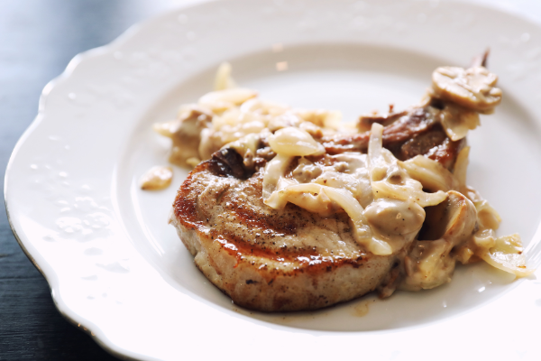 bone in pork chop topped with cream sauce on a white plate