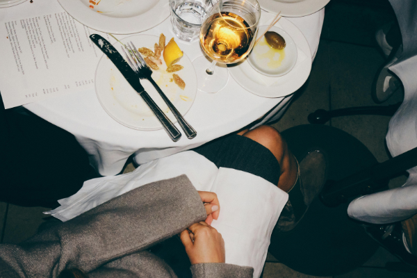 overhead image of a woman's lap at a dinner table scattered with empty dishes and wine