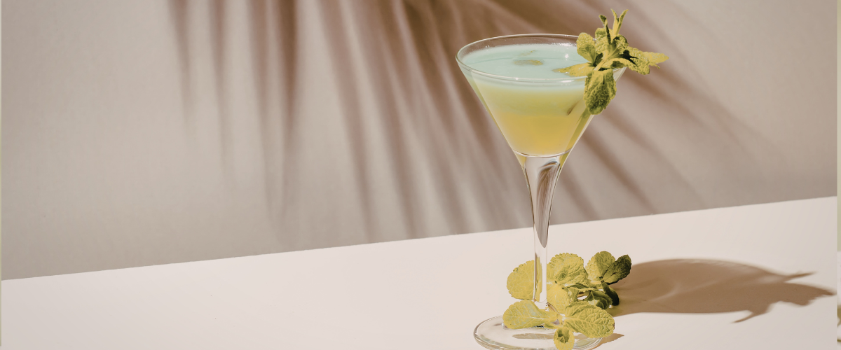 A pale green cocktail in a coup garnished with mint