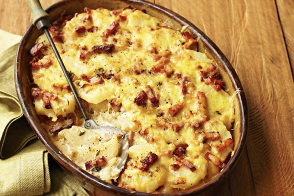 Picture of a pan of tartiflette on a wood board with a brown napkin on the side
