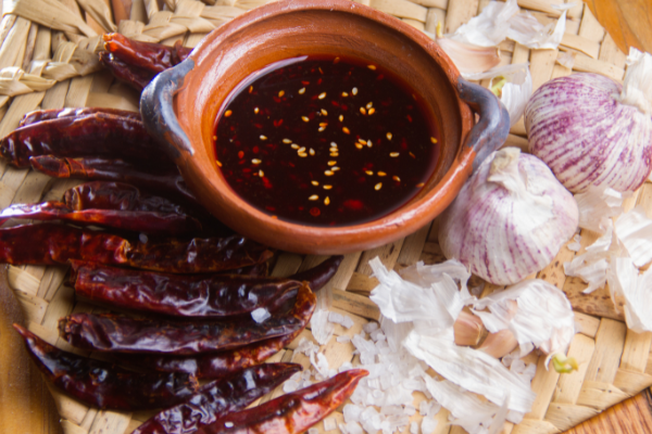 Mexican macha sauce in a terra cotta bowl surrounded by chillis and garlic