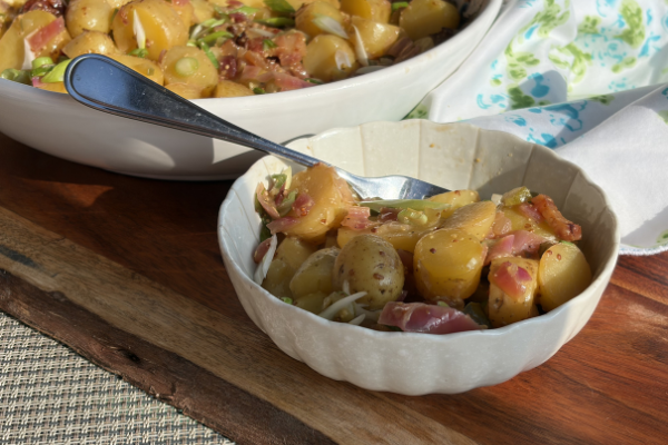 bowl of potato salad in the sun, larger serving bowl behind it
