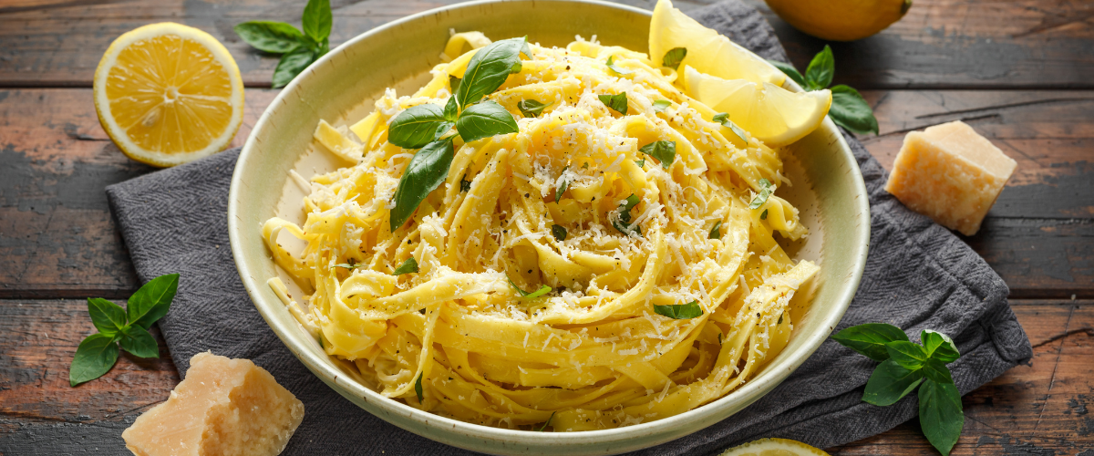 a bowl of lemon pasta on a board surrounded by lemon and basil