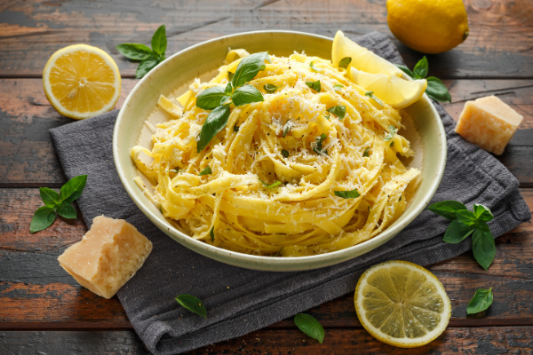 a bowl of lemon pasta on a board surrounded by lemon and basil