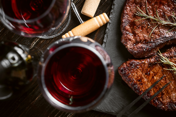 Seared steak on a board beside two glasses of dark red wine