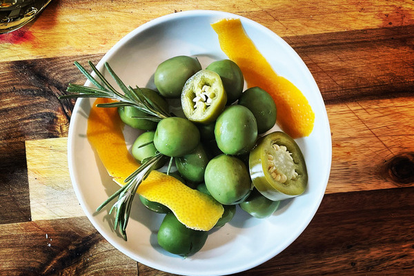 Bowl of green olives with herbs and citrus peel