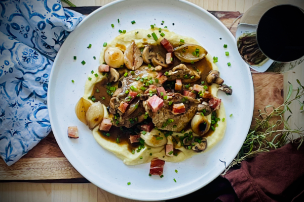 over head view of coq au vin on a white plate beside a glass of red wine