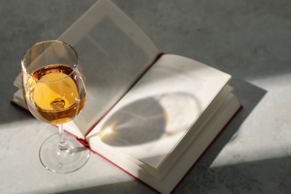 Glass of White Wine throwing a shadow on a Book on Grey Table
