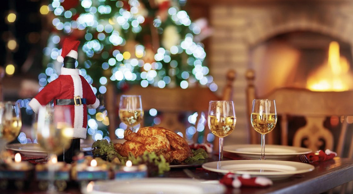 side angle of a table set with wine glasses, plates and turkey with a fireplace and christmas tree in the background