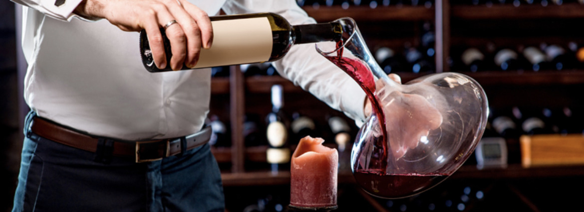 picture of a man pouring red wine into a glass decanter over a candle