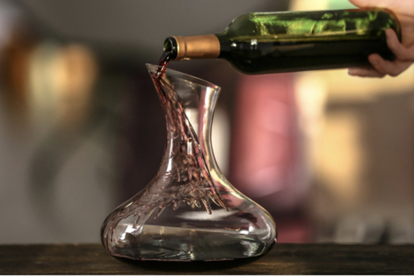 close up of a wide, glass decanter sitting on a table with red wine pouring into it