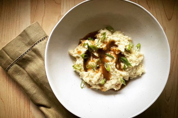 an over head view of a white bowl with a swirl of celeriac mash topped with gravy and sliced onions. A beige napkin is beside the bowl