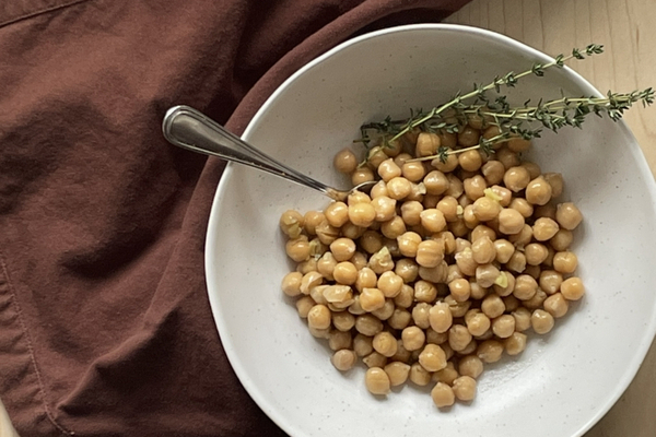 A white bowl of chickpeas with thyme scatter overtop. A brown napkin is beside the bowl.