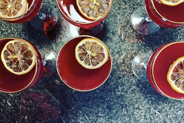 Top view of 6 bright red cocktails in coups with a dehydrated lemon wheel floating on top