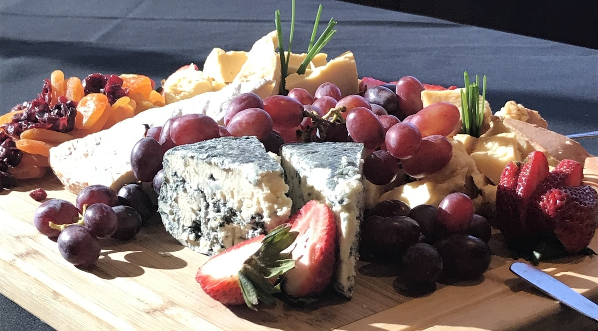 An overflowing cheeseboard filled with different cheeses, grapes and strawberries