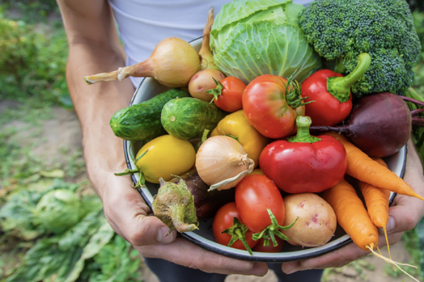 Close up of a basket overflowing with various vegetables, a strong, muscular arm holding it