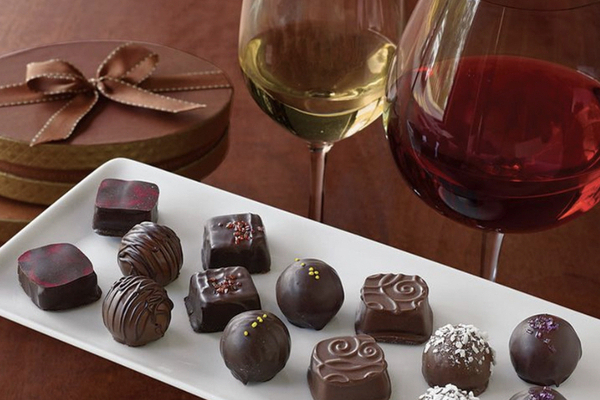 A glass of red and white wine beside a white plate filled with chocolate bonbons