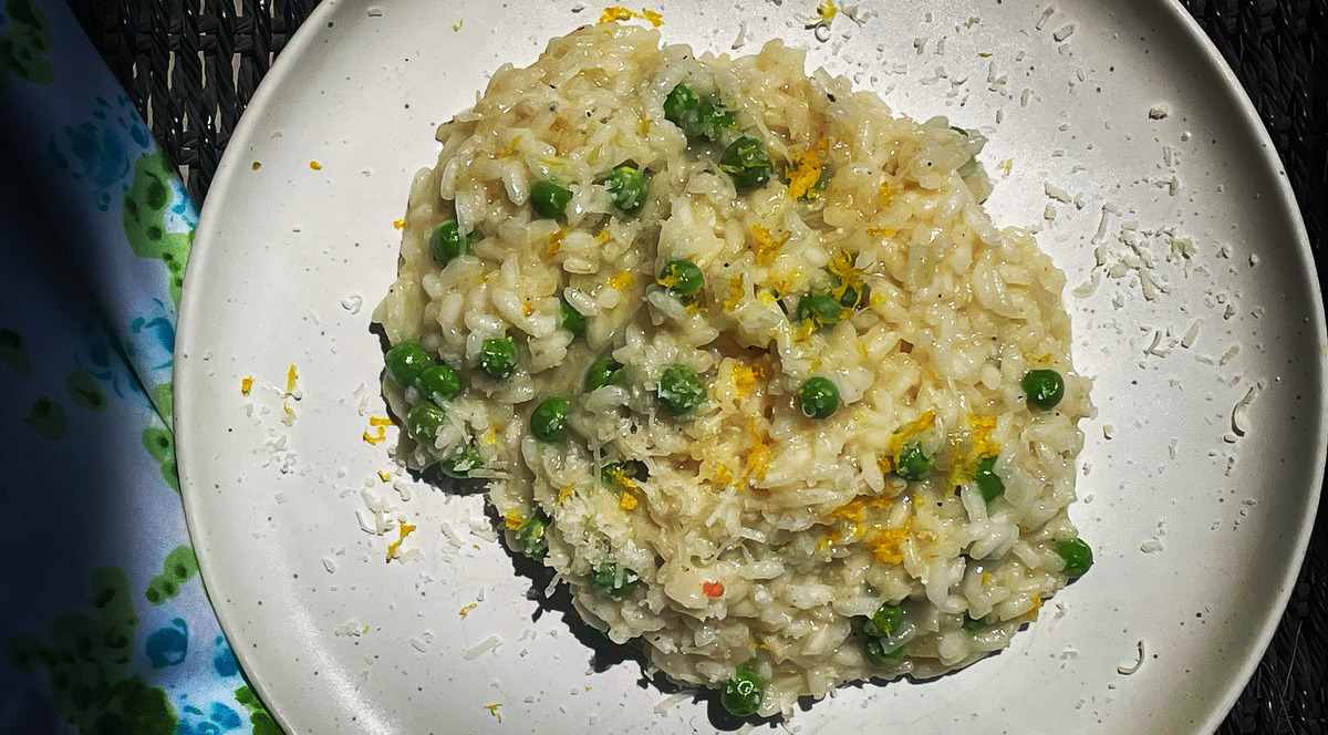 Risotto with green peas on a white plate and black table cloth. There is a floral napkin in the background.