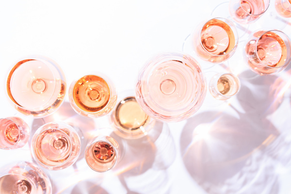a number of rosé filled wine glasses, of different shades, on a white table.