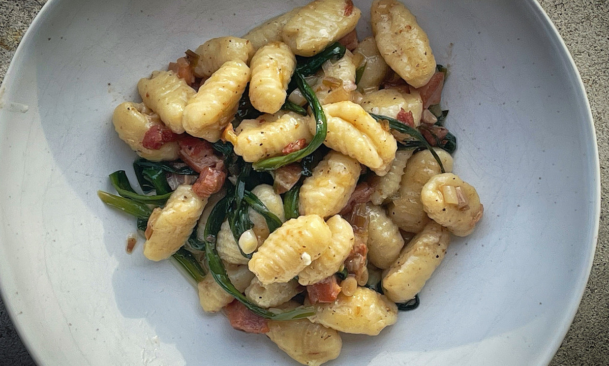 Close up on a white bowl of gnocchi green ramps laced throughout,