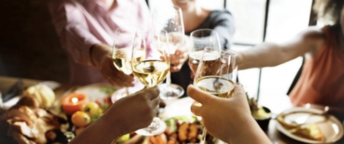 a group gathered around a dinner table clinking wine glasses filled with red and white wines in a cheers