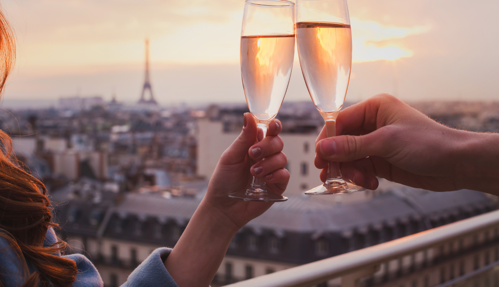 two champagne glasses clinking in the foreground against a sunset, a blurry Eiffel Tower in the distance