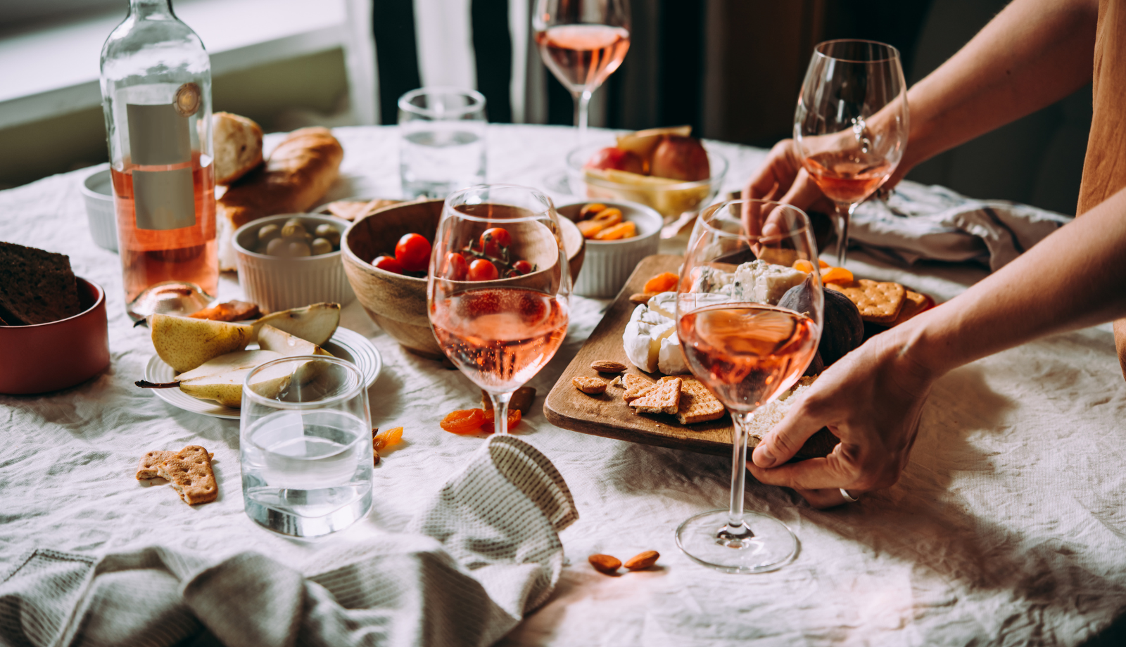 An Italian dinner table with wine and food, a woman's hands placing a tray of food on the table