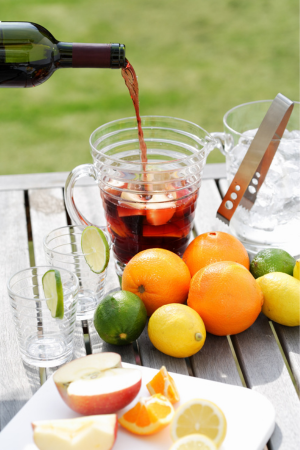 Red wine being poured into a glass pitcher surrounded by fruits