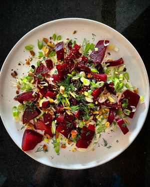 overhead view of purple beets with sliced green onion, dill and pistachio on a white circular plate on a black counter