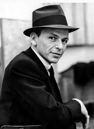 Frank Sinatra, in a fedora and suit, sitting in a chair looking over his shoulder